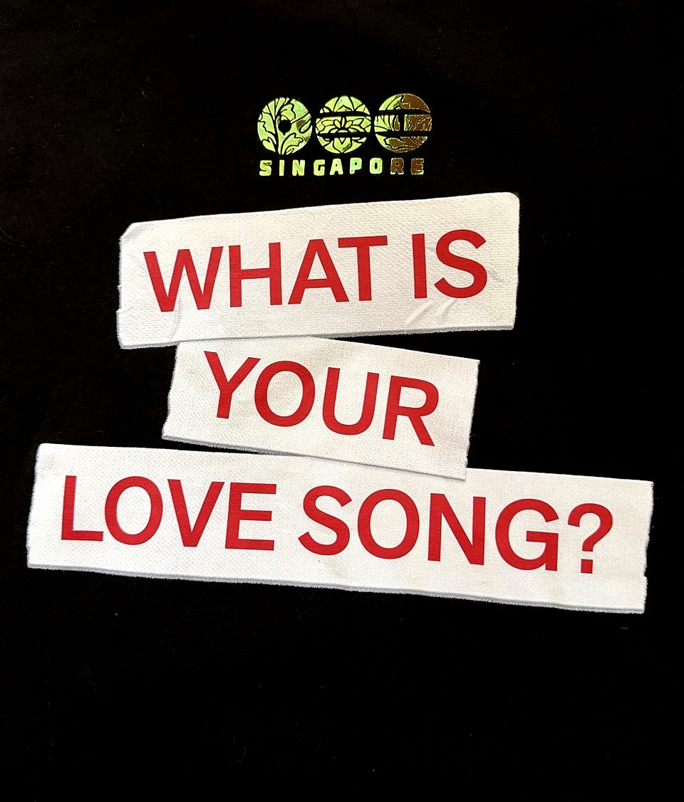 The holographic Singapore transfer pressed onto a black t-shirt, above a printed What is your love song slogan